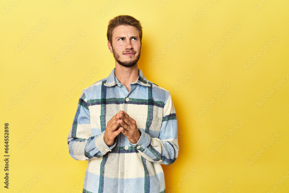 Fototapeta premium Young Caucasian man on a yellow studio background making up plan in mind, setting up an idea.