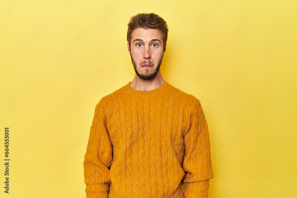 Young Caucasian man on a yellow studio background shrugs shoulders and open eyes confused. Young Caucasian man on a yellow studio background shrugs shoulders and open eyes confused.