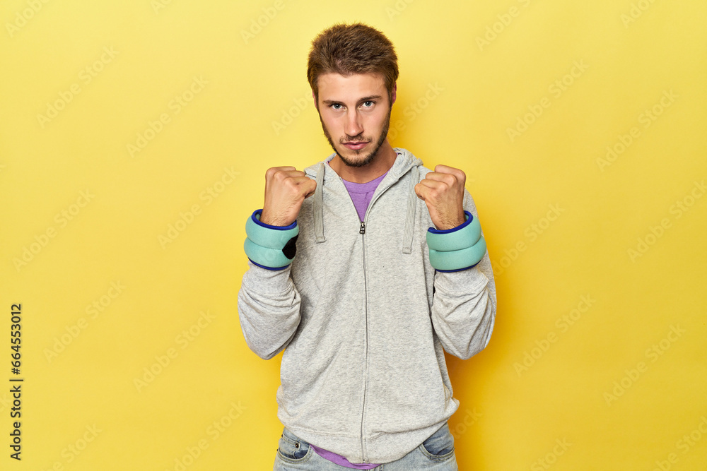 Young athlete with wrist weights boxing on a yellow studio background