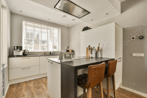 a kitchen and dining area in a modern apartment with wood flooring  white cupboards and wooden bar stools