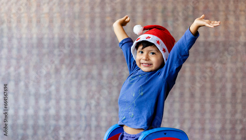Cute happy boy with a Christmas hat, and with his arms raised. Copy space.