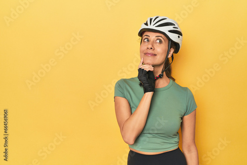 Cyclist middle aged woman with helmet and gloves posed looking sideways with doubtful and skeptical expression. © Asier