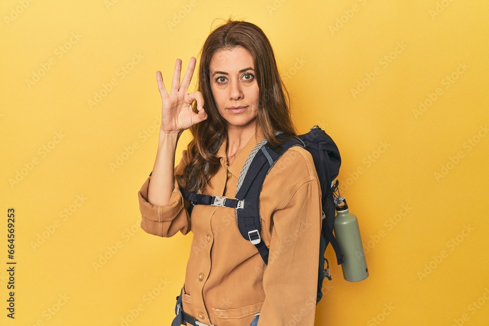 Middle aged woman prepped for hiking, yellow studio shot cheerful and confident showing ok gesture. Middle aged woman prepped for hiking, yellow studio shot cheerful and confident showing ok gesture.