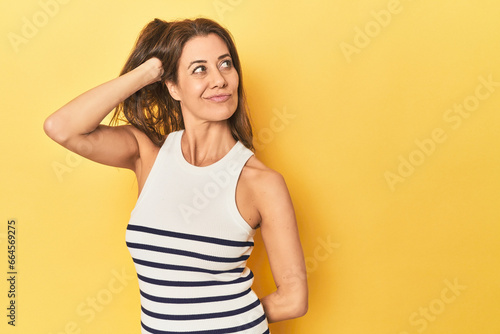 Middle-aged caucasian woman on yellow touching back of head, thinking and making a choice.
