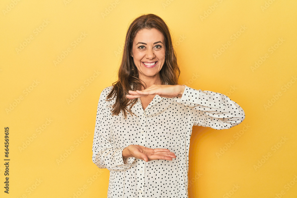 Obraz premium Middle-aged caucasian woman on yellow holding something with both hands, product presentation.