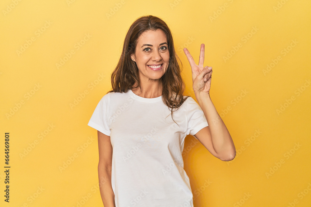 Middle-aged caucasian woman on yellow joyful and carefree showing a peace symbol with fingers. Middle-aged caucasian woman on yellow joyful and carefree showing a peace symbol with fingers.