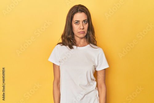 Middle-aged caucasian woman on yellow sad, serious face, feeling miserable and displeased.