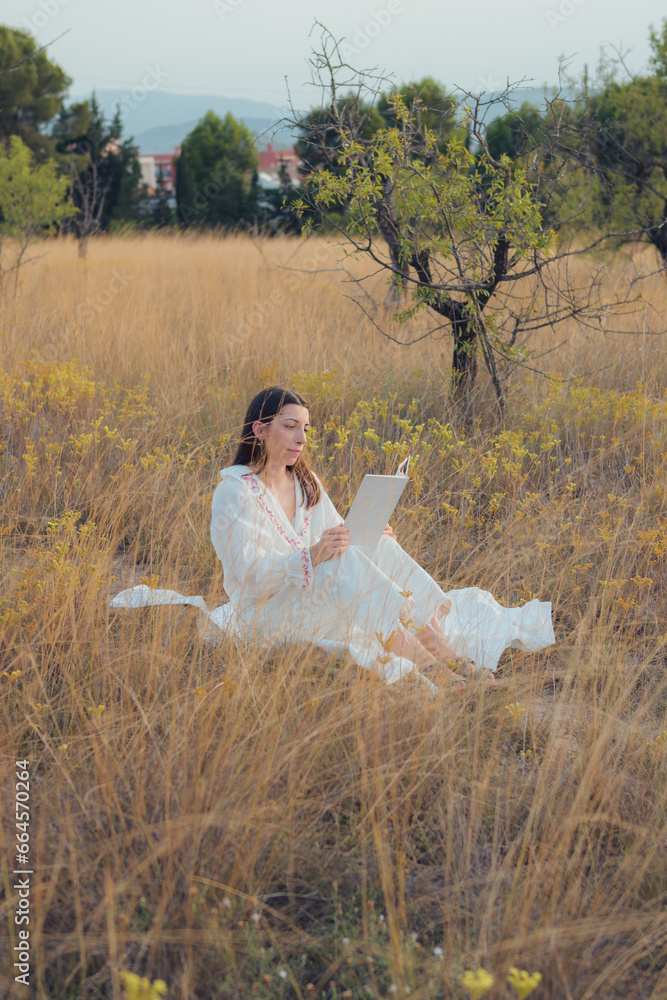 Woman with a book reading on a meadow at sunset Woman with a book reading on a meadow at sunset
