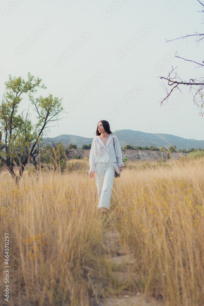 Young woman dressed in white walks through a meadow at sunset Young woman dressed in white walks through a meadow at sunset
