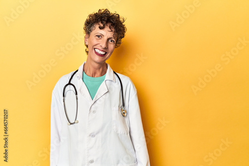 Caucasian mid-age female doctor on yellow studio happy, smiling and cheerful.