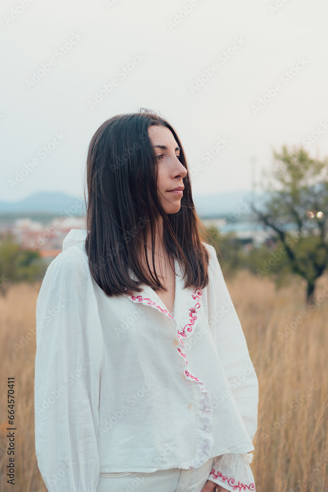 Young woman dressed in white posing on a meadow at sunset
