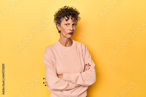 Mid-aged caucasian woman on vibrant yellow suspicious, uncertain, examining you. © Asier