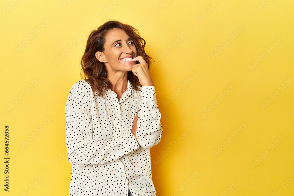 Middle-aged woman on a yellow backdrop relaxed thinking about something looking at a copy space. Middle-aged woman on a yellow backdrop relaxed thinking about something looking at a copy space.