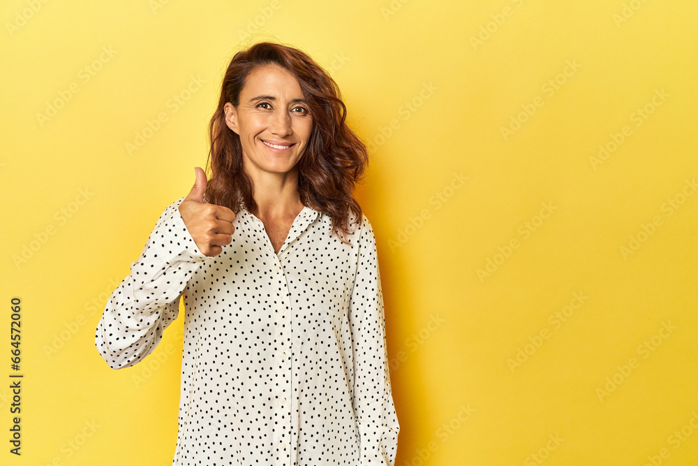 Middle-aged woman on a yellow backdrop smiling and raising thumb up Middle-aged woman on a yellow backdrop smiling and raising thumb up