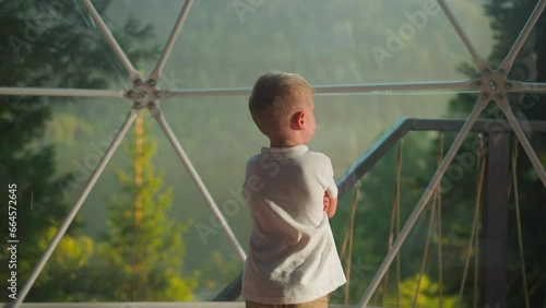 Kid looks at nature through transparent wall of tent photo