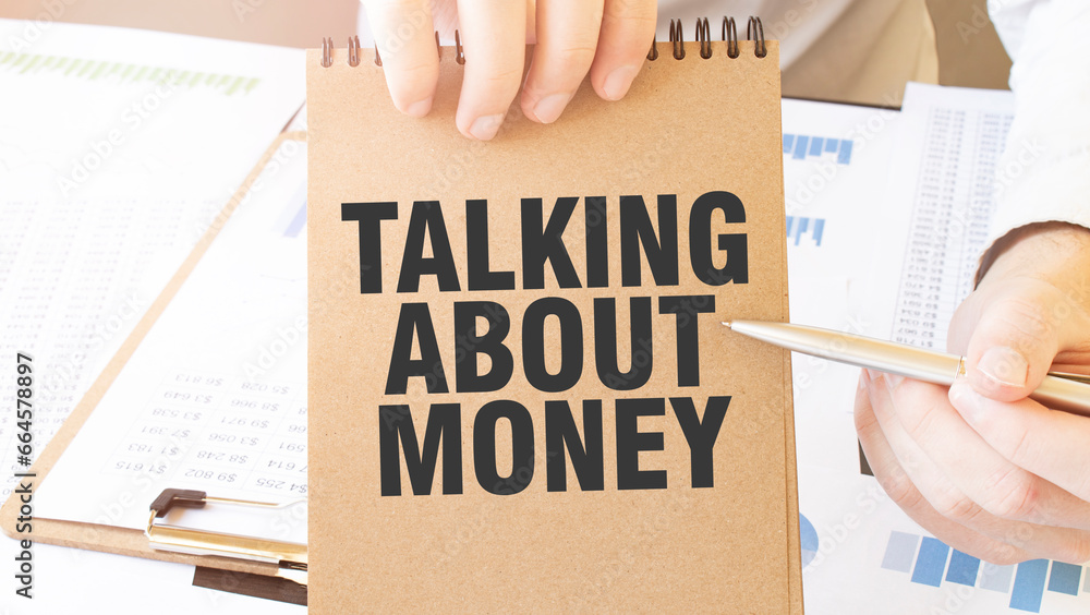 Text TALKING ABOUT MONEY on brown paper notepad in businessman hands on the table with diagram. Business concept - obrazy, fototapety, plakaty 