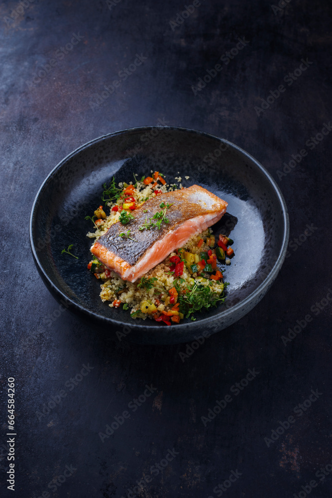 Traditional Mediterranean salmon fish fillet with vegetable cuscus served as close-up on a design bowl with copy space Traditional Mediterranean salmon fish fillet with vegetable cuscus served as close-up on a design bowl with copy space