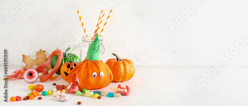 Paper pumpkins for Halloween and tasty candies on light background with space for text