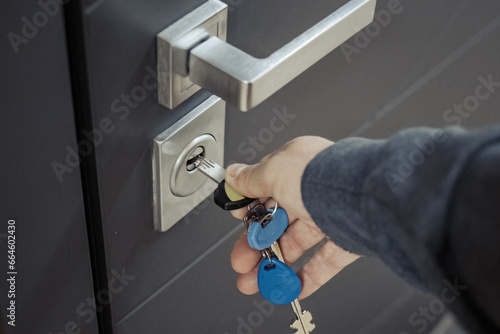 hand with key opening or closing gray entrance door