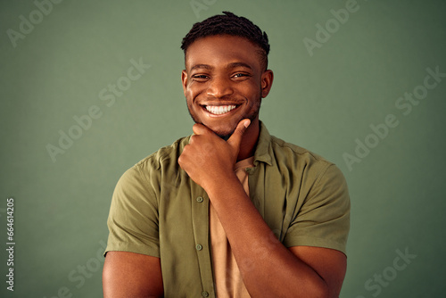 New ideas and thoughts. Portrait of smiling african american man keeping hand near chin and looking at camera over green background. Thoughtful guy in khaki shirt searching for inspiration in studio. photo