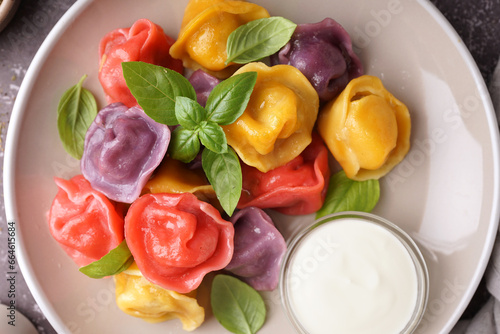 Plate of boiled colorful dumplings with basil and sour cream on dark table, closeup