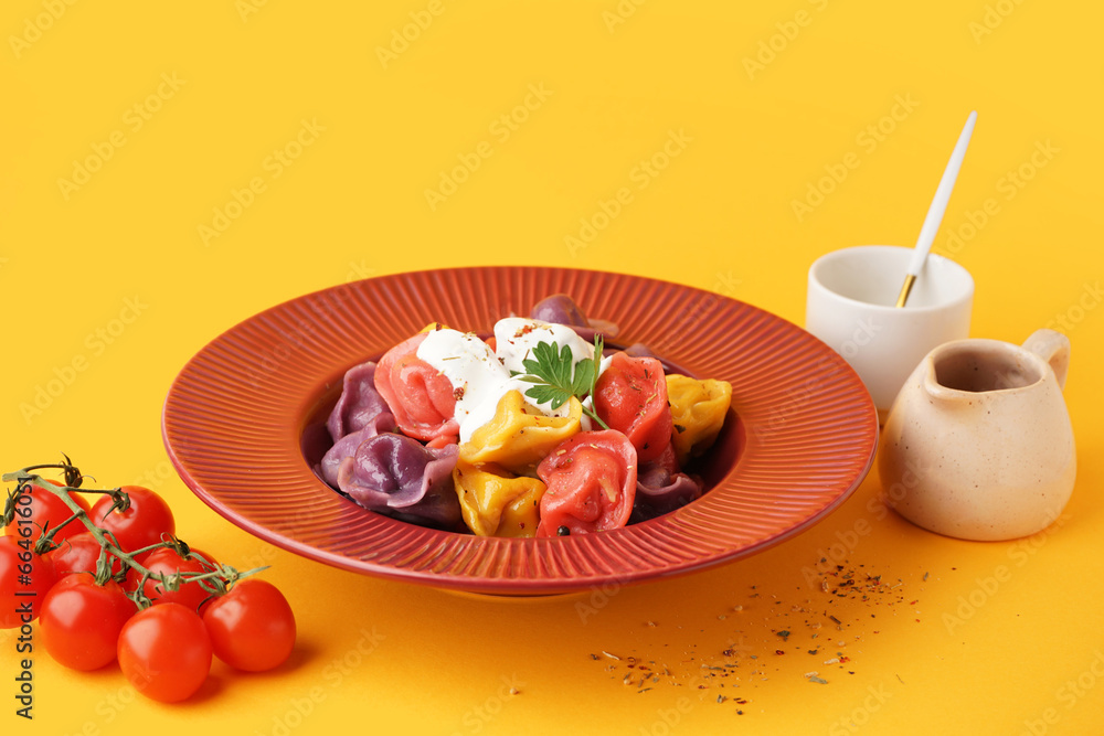 Plate of boiled colorful dumplings with sour cream and parsley on orange background Plate of boiled colorful dumplings with sour cream and parsley on orange background