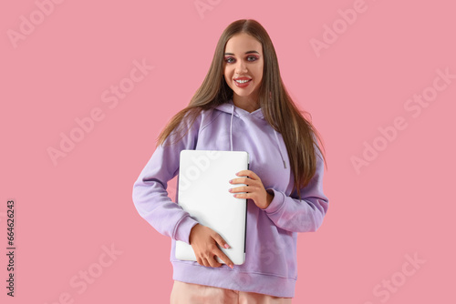 Young woman in hoodie with laptop on pink background