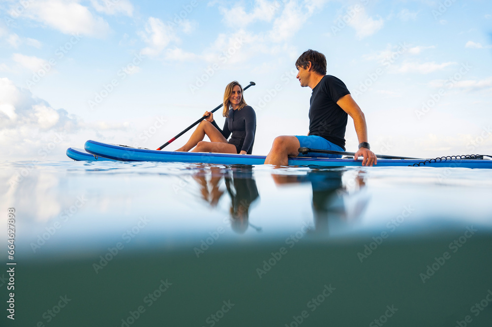 Young man and woman on the sea with a paddle surf board - obrazy, fototapety, plakaty 