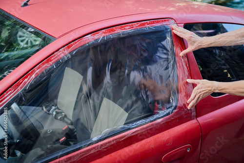 A man puts a polyethylene cellophane on the window of a red car