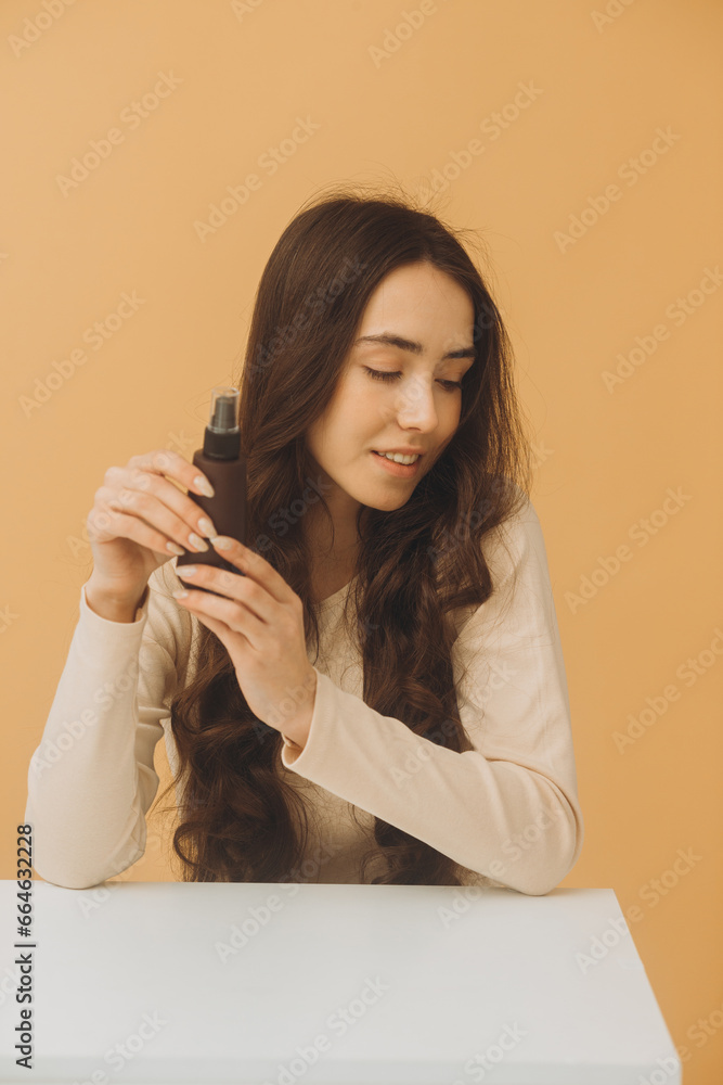 Pretty woman holding bottle of cosmetics isolated on beige background. Pretty woman holding bottle of cosmetics isolated on beige background.