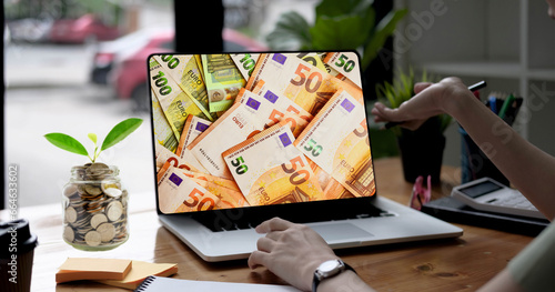 Mujer exitosa observando en su laptop los miles de euros que ha ganado con su venta online. Las monedas de su frasco se multiplican como una planta que no para de crecer. Su mano recibe la ganancia. photo