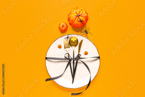 Beautiful table setting for Halloween celebration with pumpkins on orange background