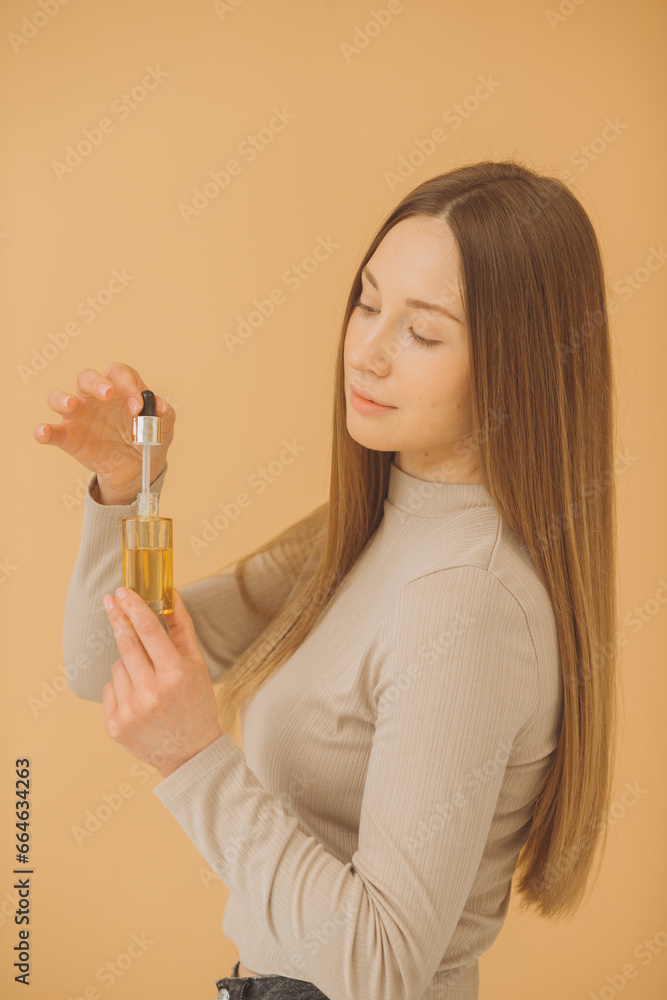 A beautiful girl poses with face serum or hair oil on a beige background. A beautiful girl poses with face serum or hair oil on a beige background.