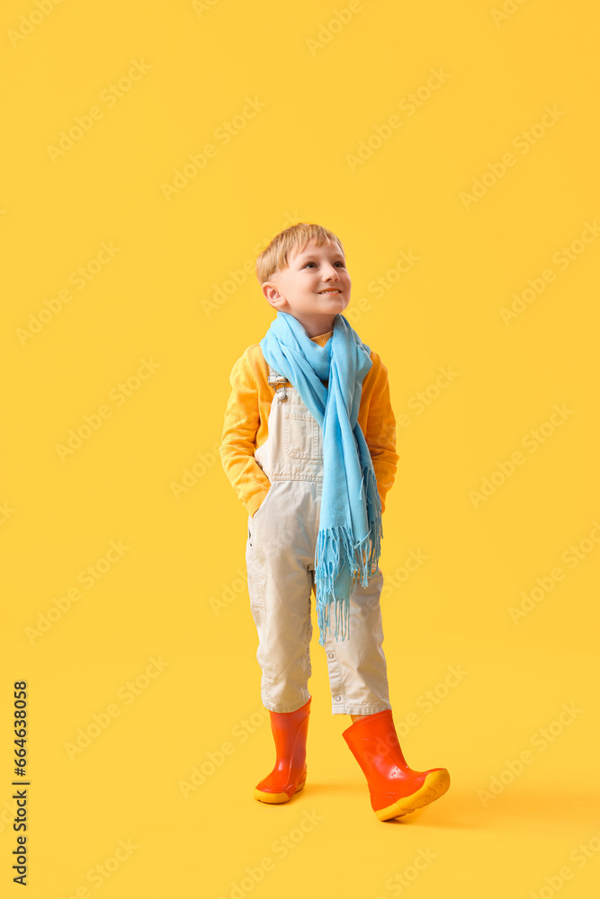 Little boy in rubber boots on yellow background