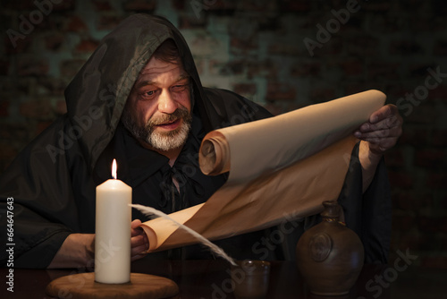 Emotional portrait of an elderly monk, by candlelight reading a message on parchment.