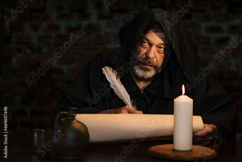 An old monk in a cell by candlelight writes a message on parchment with a goose quill, a scribe of holy scriptures.