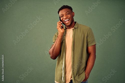 Always in touch. Overjoyed handsome guy in casual attire having mobile conversation over green background. African american male person communicating on modern smartphone in studio.