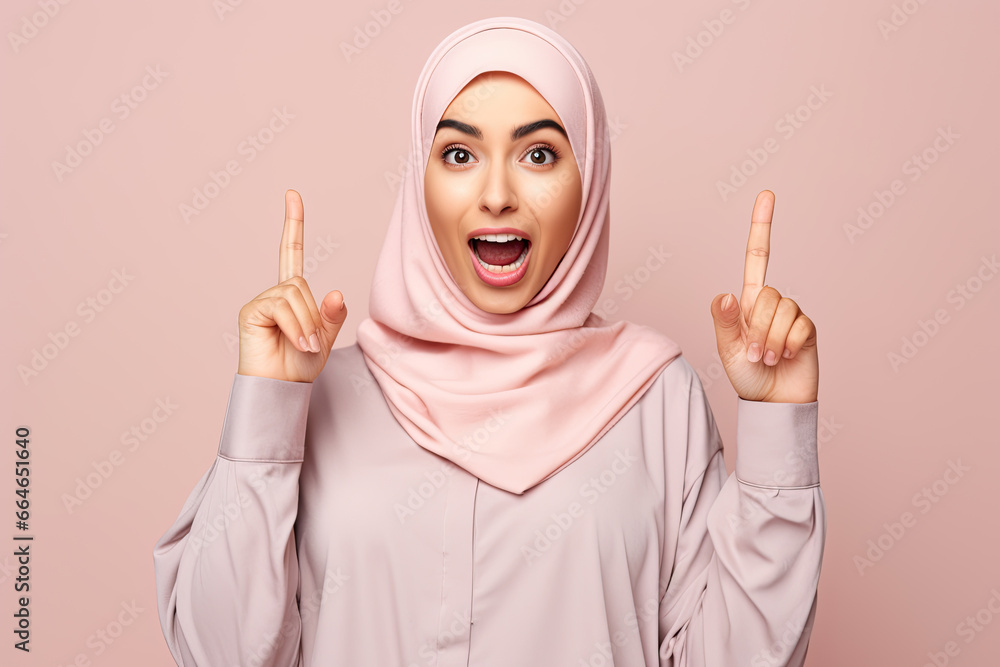 A positive muslim woman wearing pink hijab pointing to the copyspace and looking to the side A positive muslim woman wearing pink hijab pointing to the copyspace and looking to the side