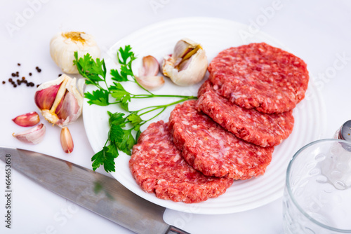 Plate of raw formed hamburger patties ready for cooking with fresh fragrant parsley, spicy garlic and allspice. Popular dish concept
