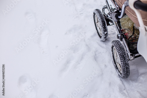 Stroller wheels for baby with big treads on snowy road in park in winter