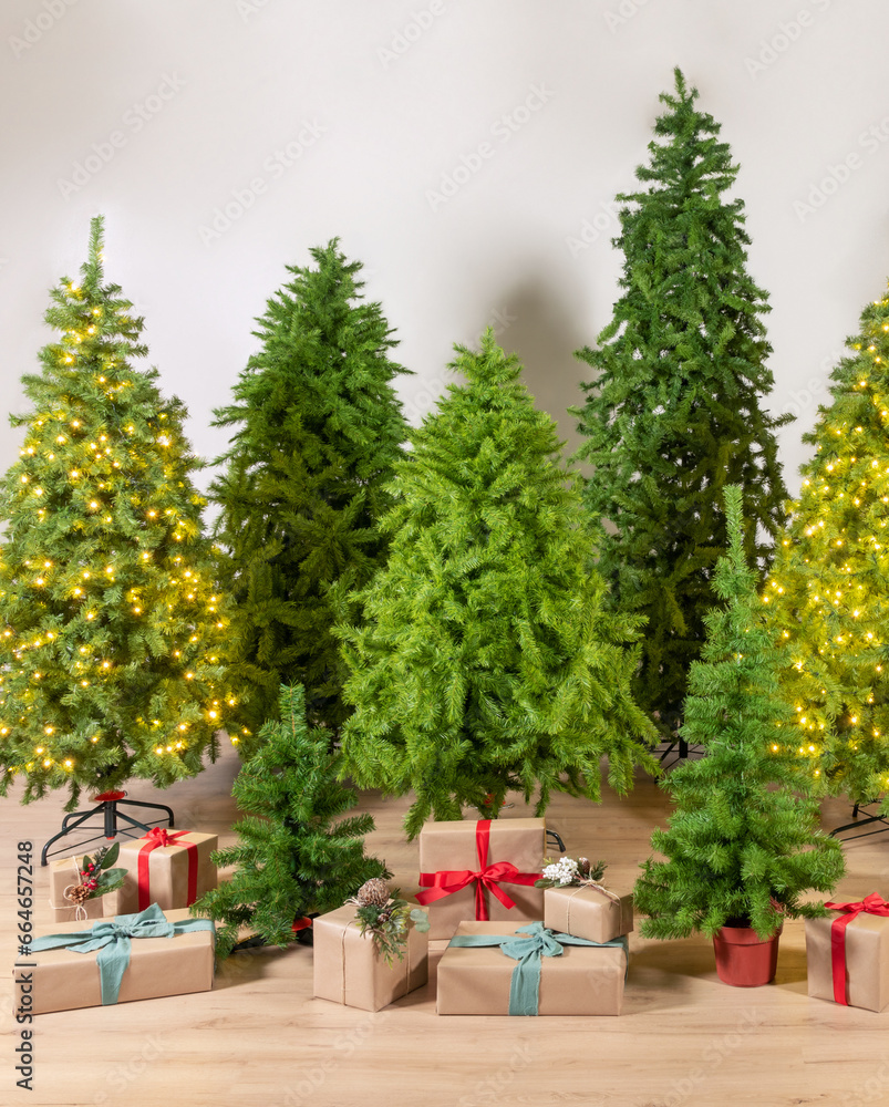 Vibrant array of Green Artificial Christmas trees, both lit with golden fairy lights and undecorated, surrounded by elegantly wrapped presents on a wooden floor, festive spirit of the holiday season.