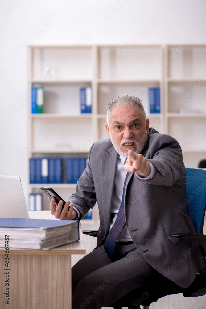 Old male employee speaking by phone at workplace Old male employee speaking by phone at workplace