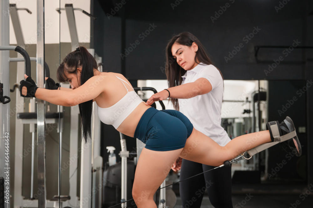 Fototapeta premium Trainer assisting a girl to correctly do a gluteal exercise in the gym.