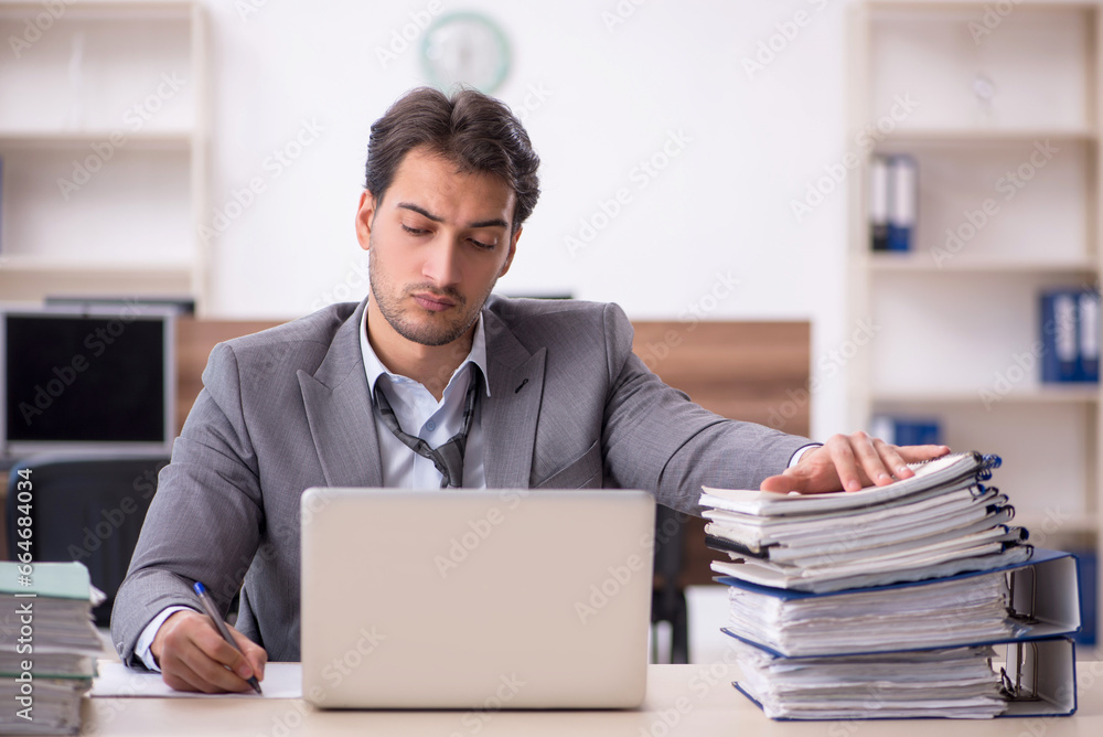 Young male employee unhappy with excessive work in the office Young male employee unhappy with excessive work in the office