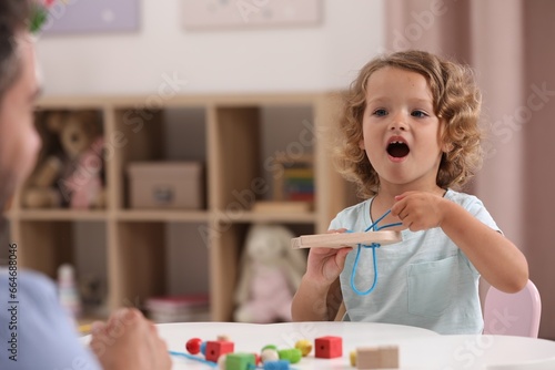 Motor skills development. Father and little daughter playing with wooden lacing toy at white table indoors