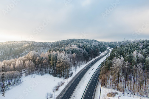Beautiful aerial view of snow covered fields with a two-lane road among trees. Rime ice and hoar frost covering trees. Scenic winter landscape in Lithuania.