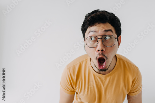 Funny asian man wow and shocked face wear yellow t-shirt isolated o n white.