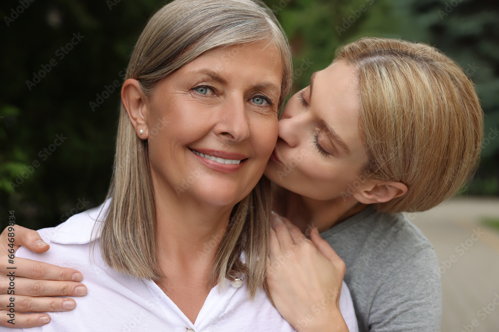 Daughter kissing her mature mother on cheek outdoors Daughter kissing her mature mother on cheek outdoors
