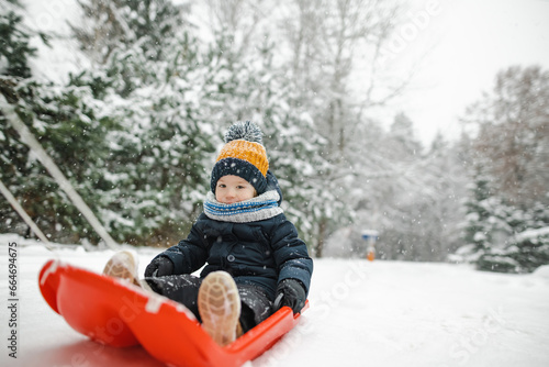 Funny toddler boy having fun with a sleigh in beautiful winter park. Cute child playing in a snow.