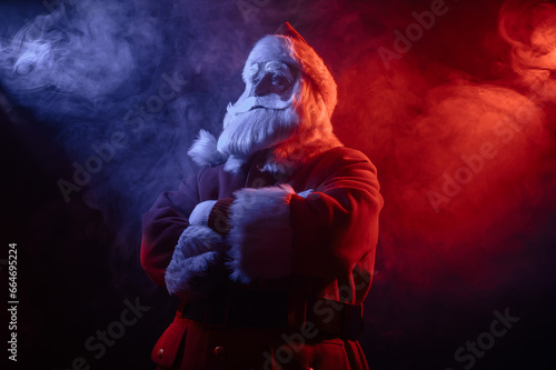 Santa Claus stands with his arms crossed on his chest in blue red neon light and smoke.  photo